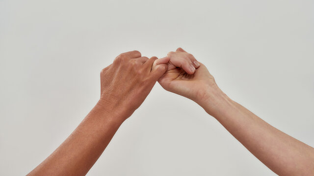 Close up of two hands hook little finger together to promise or asking for asking for reconciliation isolated over light background