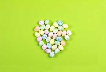 Flat lay composition of Happy Easter holiday concept. Colorful heart from little pastel eggs on green background. top view