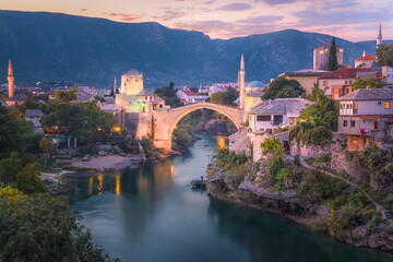 A beautiful sunset view of the iconic Stari Most bridge, Neretva River and old town of Mostar, Bosnia and Herzegovina with mountain backdrop.