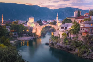 Papier Peint photo Stari Most A beautiful sunset view of the iconic Stari Most bridge, Neretva River and old town of Mostar, Bosnia and Herzegovina with mountain backdrop.