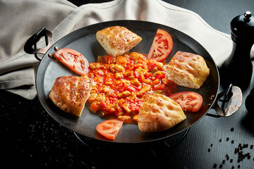 Turkish chicken goulash in red sauce with bell pepper and traditional buns in a metal dish on a black background. Close up, selective focus