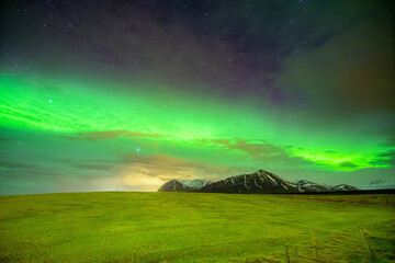 auroras boreales y algunas nubes sobre una montaña con nieve y un prado verde en Islandia