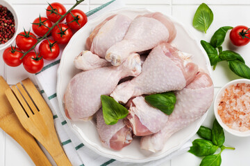 Raw chicken legs with, tomato cherry, herbs, basil and spices, on white marble background, copy space top view. Cooking healthy diet lunch concept.