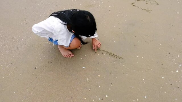 Asian child girl wearing a white shirt and jeans writing I love on the sand.