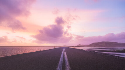 An empty road straight ahead near Dyrholaey in Southern Iceland with a colourful sunset. 