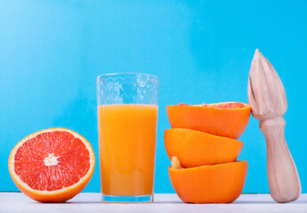 Blood orange juice freshly squeezed in the drinking glass with pulp, wooden juicer and the fruit peels against the blue colorful background © kcuxen