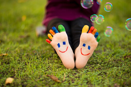 Child feet with painting smiles lying on green grass with bubble 