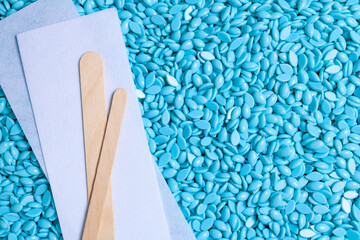 Background texture of blue depilatory wax and wooden spatulas. Depilation wax granules. Epilation,...
