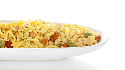 Delicious Khatta Meetha in a white  ceramic ova bowl, made with peanuts, sugar, raisins, and besan sev. Pile of Indian spicy snacks (Namkeen), under backlight, side view, against the white background.