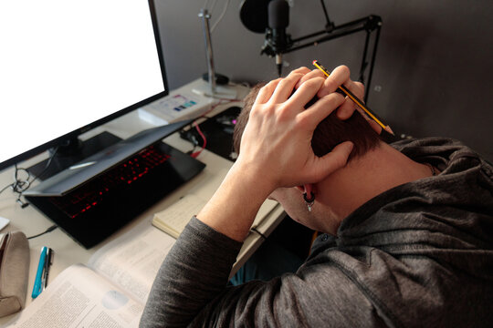 Hombre joven caucásico enfrente del ordenador con las manos a la cabeza agobiado, estudiando desde casa 