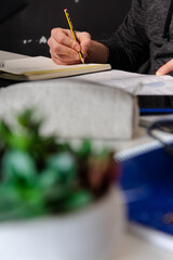 Hombre cauc&aacute;sico escribiendo en una libreta con un l&agrave;piz con cosas de escritorio fuero de foco delante.