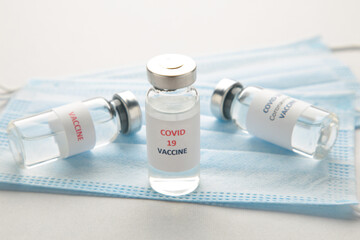 Coronavirus COVID-19 vaccine vials and hygiene protective face mask on grey background.