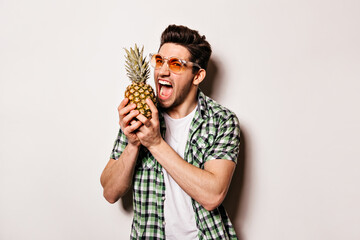 Cheerful guy in white T-shirt, green shirt and bright sunglasses wants to bite off piece of...