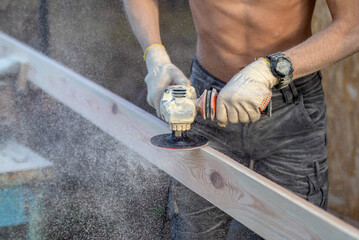 sanding the board with a hand-held power tool. Street, board clamped in a vise, small sawdust.