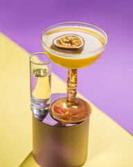 yellow tropical cocktail with passion fruit and shot on a background of tropical plant leaves and sun shades. Color background