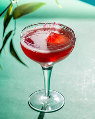 red tropical cocktail with ice in the form of a crystal on a background of foliage and shadows from sunlight.Green background