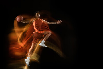 Carry on winning. Young arabian muscular basketball player in action, motion on black background in...