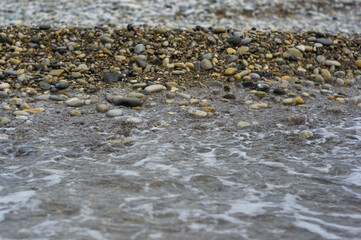 pebble stones on the sea beach, the rolling waves of the sea with foam