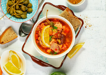 Home cooked solyanka meat soup served with lemon, olives and capers, top view