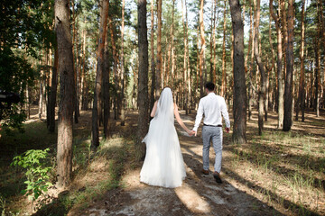 Happy bride and groom holding hands and walking in forest on wedding day. Wedding couple in love, newlyweds, copy space