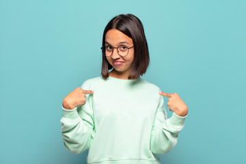 young hispanic woman looking proud, arrogant, happy, surprised and satisfied, pointing to self,...