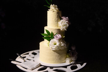 Elegant three-tiered wedding or birthday cake decorated with fresh flowers on table in restaurant,...