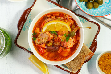 Home cooked solyanka meat soup served on a tray with lemon, olives and capers, top view