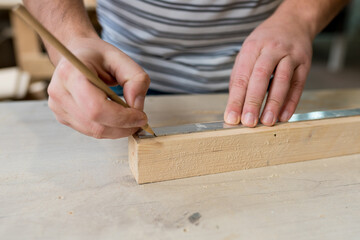 Man carpenter measuring a wooden board with a ruler with scale in workshop. Joinery work on the production and renovation of wooden furniture. Small Business Concept