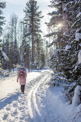 A girl in a red jacket walks through a snow-covered forest