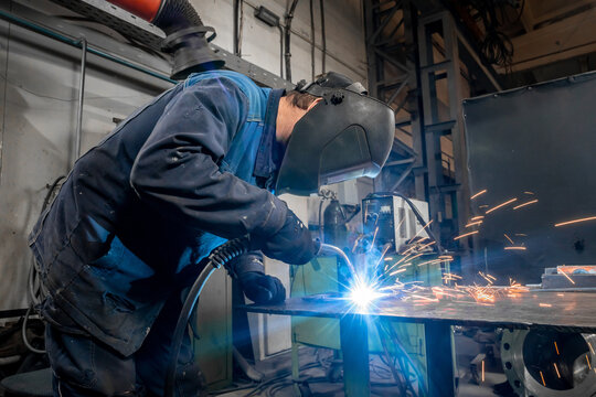 welding work at a metalworking plant. A helmeted welder welds a metal part on a welding table