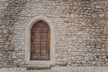 Ancient wooden arcade door with iron rivets at wall of old building. Heavy closed door on a stone wall of a medieval fortress, made of riveted wood planks. Small back door to Wawel castle in Krakow.