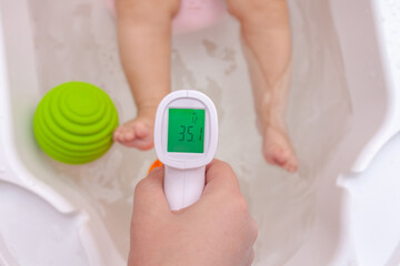 Comfortable water temperature in the bathroom. female hand with infrared thermometer checks the...