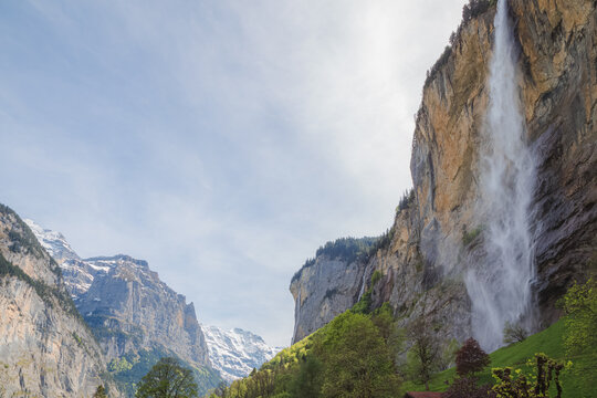 Lauterbrunnen village centre from the main street Dorf with Staubbachfall waterfall providing a dramatic backdrop on a clear spring afternoon.