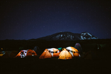 Rangée de tentes éclairées orange au sommet du Kilimandjaro la nuit visible en arrière-plan