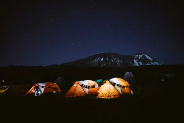 Cercles muraux Kilimandjaro Rangée de tentes éclairées orange au sommet du Kilimandjaro la nuit visible en arrière-plan