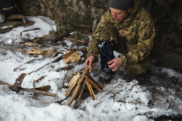 Traveller makes a fire to warm up on a frosty winter day, finding shelter from the wind next to the rock, close-up.