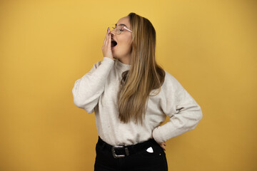 Fototapeta premium Pretty woman with long hair bored yawning tired covering mouth with hand. Restless and sleepiness against yellow wall