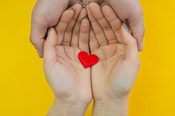 Hands on a yellow background with a heart, love. Selective focus.