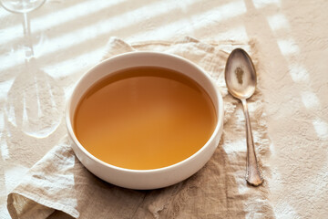 A bowl of beef bone broth on a bright background, with sunlight