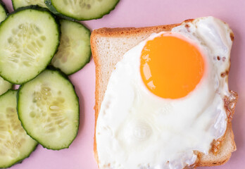 toast with egg on a plate. Fresh cucumbers. slice of white bread on a pink background. sandwich. breakfast with fried egg. High quality photo