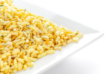 Crunchy Murmura in a white ceramic square plate made with Puffed Rice and Curry leaves. Pile of Indian spicy snacks (Namkeen)  under backlight side view against the white background.