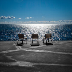 Tres sillas publicas vac&iacute;as frente al mar al atardecer