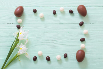 Naklejka na ściany i meble Easter chocolate eggs and flowers on green wooden background