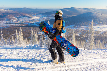 Fototapeta na wymiar A male snowboarder holds a blue snowboard and looks up at the sky on a sunny frosty day