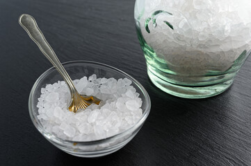 Glass jar and bowl of sea salt on black background