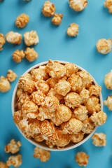 Caramel popcorn in a white glass cup with scissors on a blue background