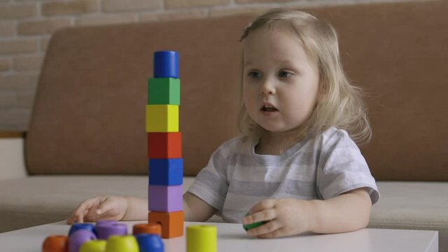 Little girl playing wooden geometrical figures on the table. Sorting rainbow cubes. Hand held Close Up Shot.