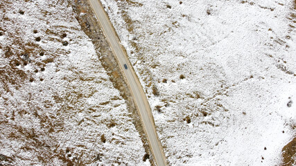 Aerial drone view of road in idyllic winter landscape. Car traveling on snowy winding road on mountain.