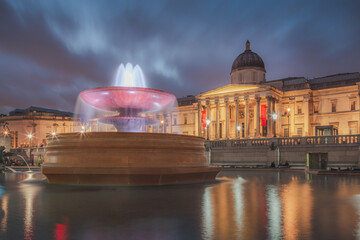 A fountain in Trafalgar Square is lit at night in front of the National Gallery in London, England,...