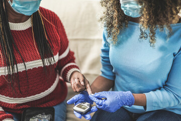 Fototapeta premium Nurse woman takes blood from a senior african patient for the diabetes exam while wearing protective face mask for coronavirus outbreak